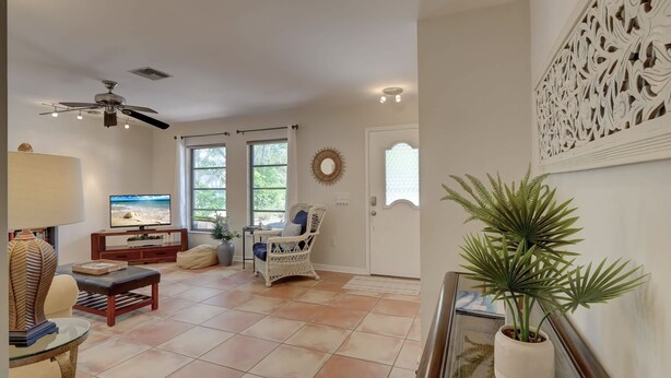 A living room with a television, a ceiling fan, a wicker chair, and a potted plant. - A Quaint and Serene Neighborhood in North Naples (Naples)