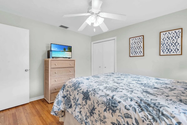 A bedroom with a bed, a television on a dresser, a ceiling fan, and two wall art pieces. - A Quaint and Serene Neighborhood in North Naples (Naples)