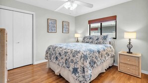 A bedroom with a bed, two bedside lamps, a ceiling fan, a wicker side table, and a door. - A Quaint and Serene Neighborhood in North Naples (Naples)