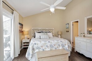 Een slaapkamer met een bed, nachtkastjes, een dressoir, een plafondventilator en een groot raam met gordijnen.