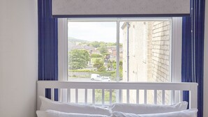 Een slaapkamer met een raam dat uitkijkt op een straat en gebouwen.