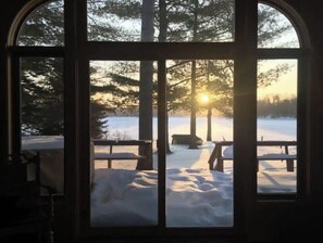 A view through a window with a snowy landscape, trees, and a bench.