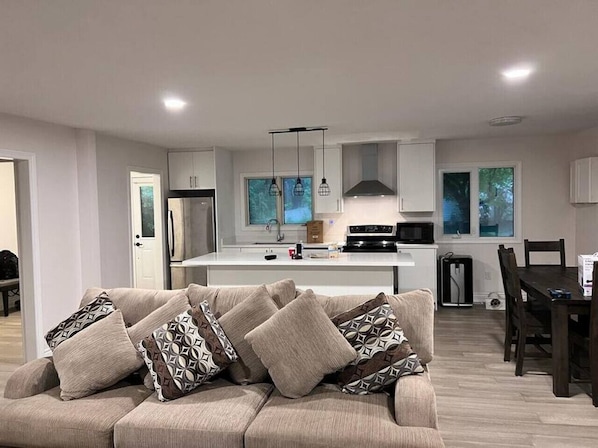 A modern living room with a sofa, a dining table, and a kitchen in the background.