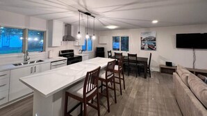 Eine moderne Küche mit einer zentralen Kochinsel, einem Essbereich mit Stühlen, einem Sofa und einem an der Wand montierten Fernseher.