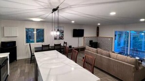 Eine moderne Küche mit einer zentralen Kochinsel, Essbereich mit Stühlen, einer Couch und einem an der Wand montierten Fernseher.