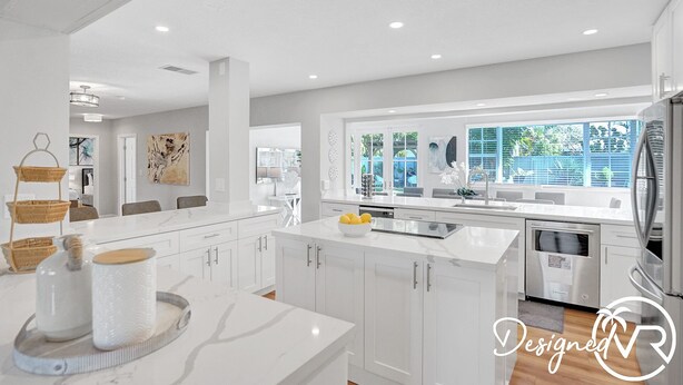 A modern kitchen with white cabinetry, a large island, and a view of the outdoors through large windows. - 8BR Family Resort with Pool & Playground (Pompano Beach)