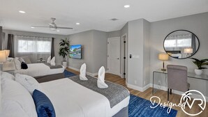 A hotel room with two beds, a desk, a chair, a ceiling fan, a large window, and a painting on the wall. - 8BR Family Resort with Pool & Playground (Pompano Beach)
