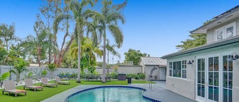 A backyard with a swimming pool, lounge chairs, and a dining area.