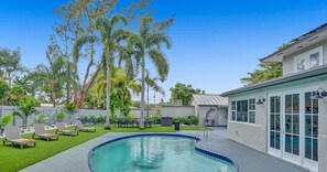 A backyard with a swimming pool, lounge chairs, and a dining area.