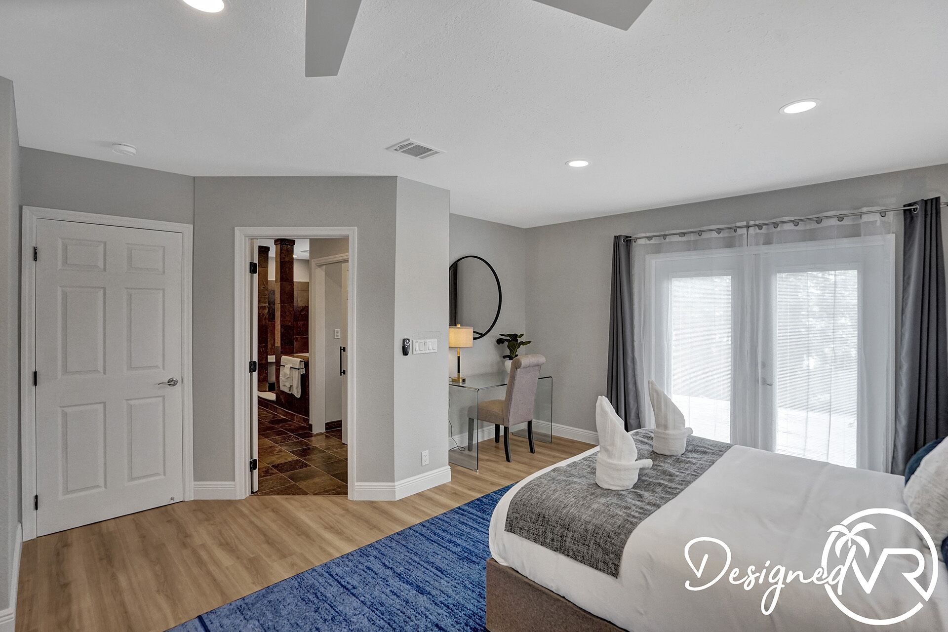 Una habitación de hotel moderna con cama, escritorio, espejo y baño visible a través de una puerta abierta.