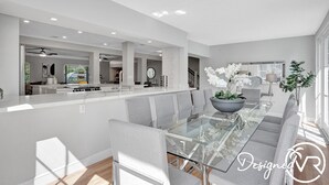 A modern kitchen with a central island, grey upholstered chairs, and a glass dining table. - 8BR Family Resort with Pool & Playground (Pompano Beach)