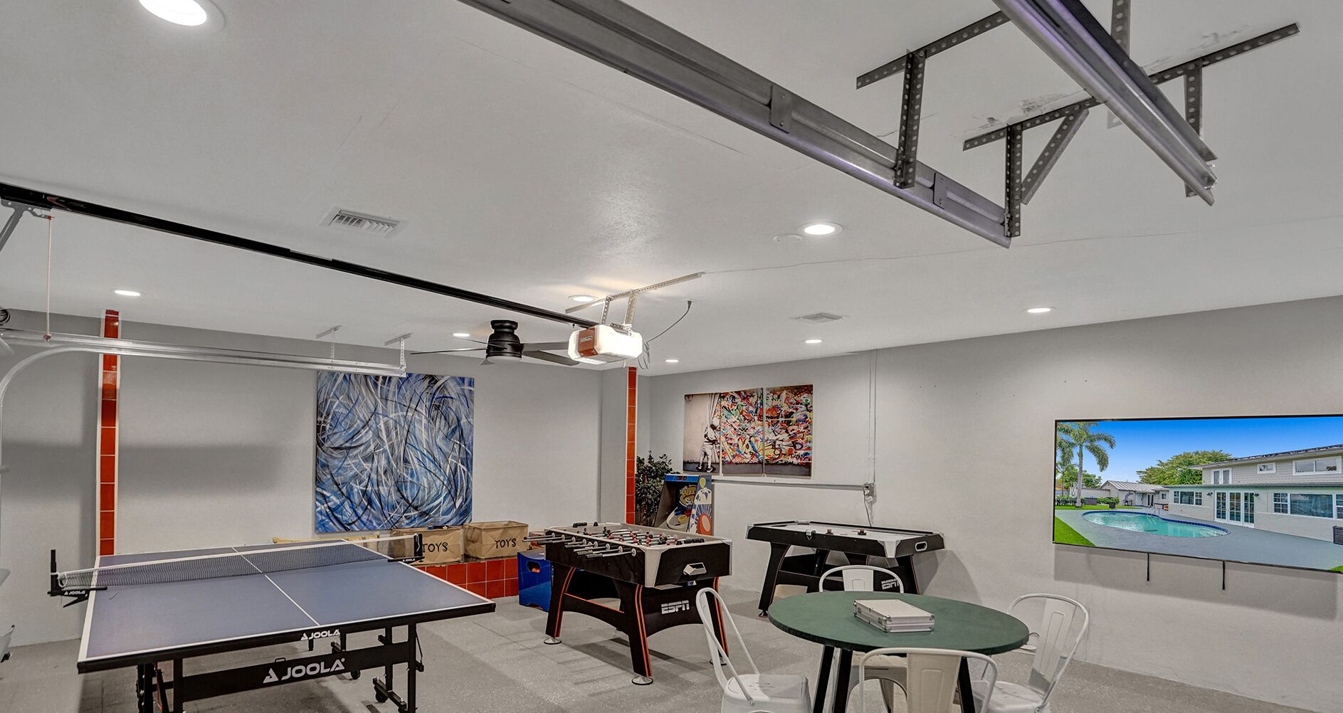 A room with a ping pong table, foosball table, and a projector screen.
