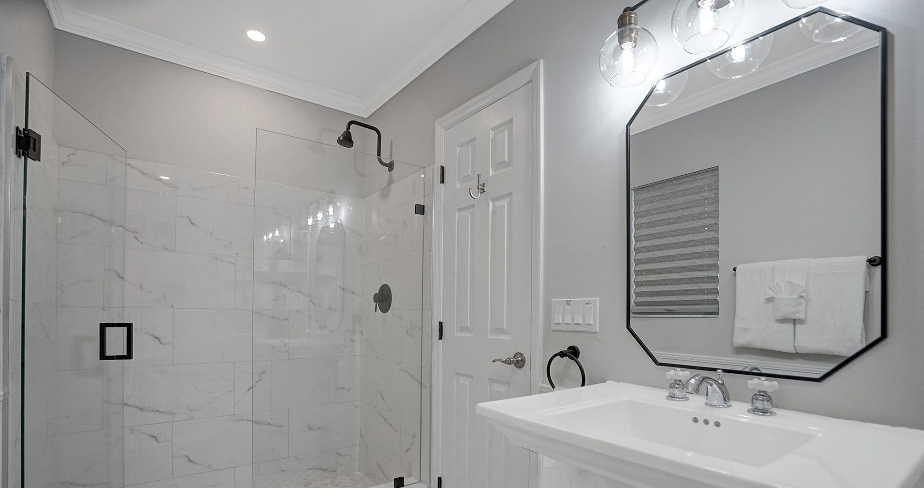 A modern bathroom with a glass shower enclosure, a white sink, and a large mirror.