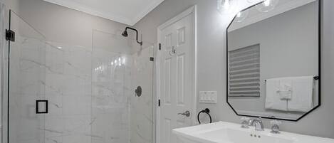 A modern bathroom with a glass shower enclosure, a white sink, and a large mirror.