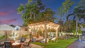 A backyard with a wooden pergola, outdoor seating, a fire pit, and a pool. - 8BR Family Resort with Pool & Playground (Pompano Beach)
