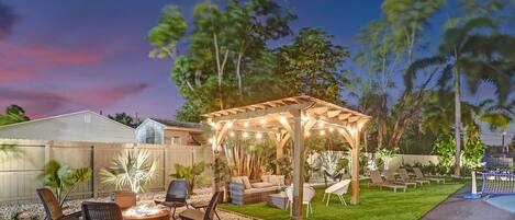 A backyard with a wooden pergola, outdoor seating, a fire pit, and a pool.