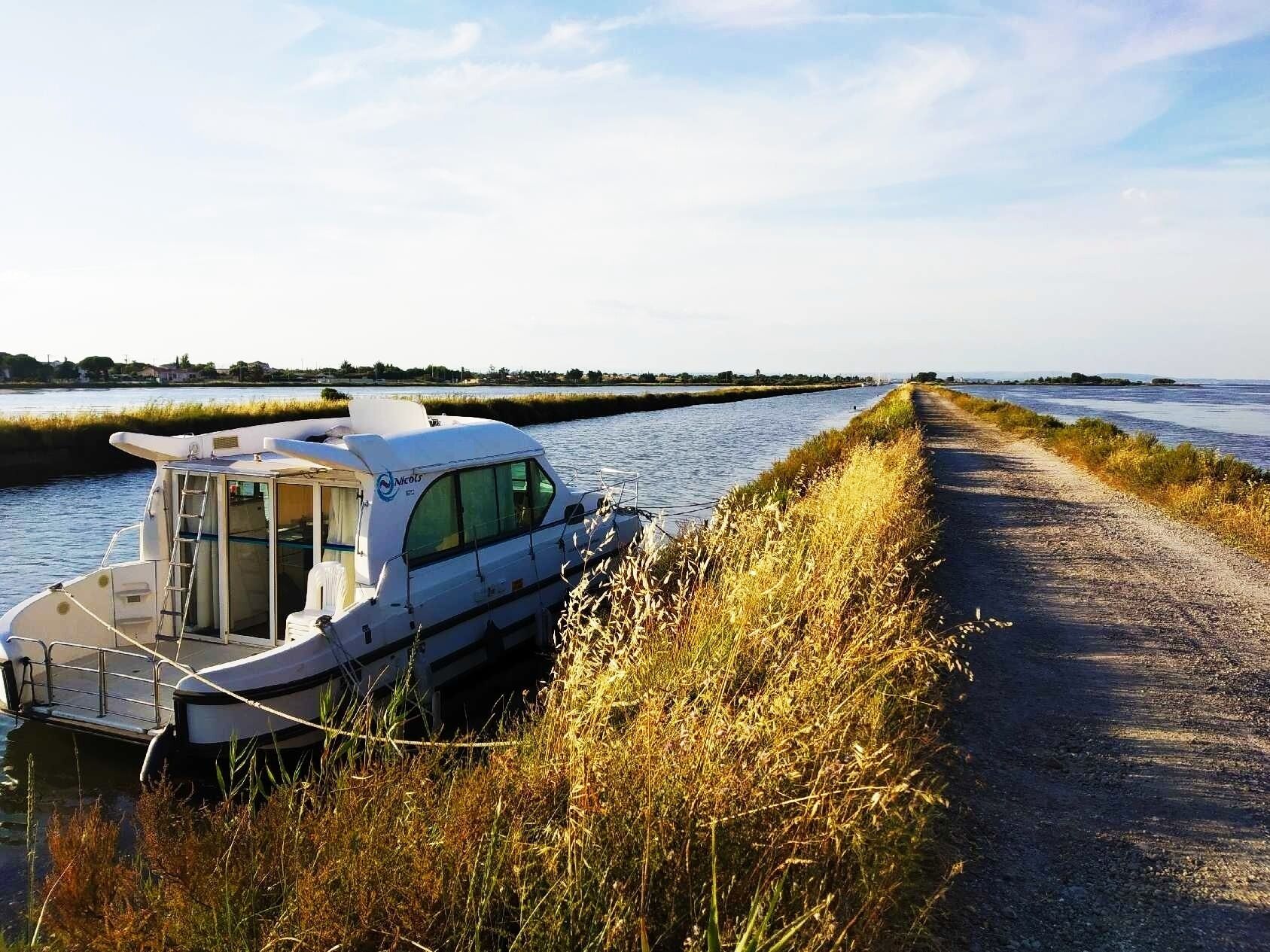 A boat docked at a narrow waterway with a gravel path beside it.