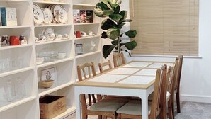 A dining area with a white table and chairs, surrounded by white shelving units filled with dishes and glassware. - Impeccable 2 Bedroom House in Bicester (Bicester)