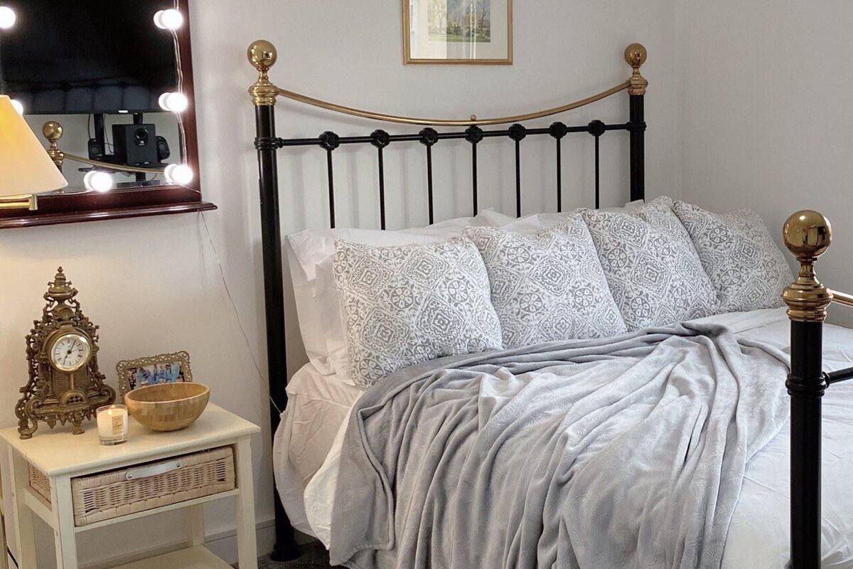 Un lit bien fait, agrémenté d’oreillers à motifs, une table de chevet avec une horloge, une bougie et un bol décoratif.