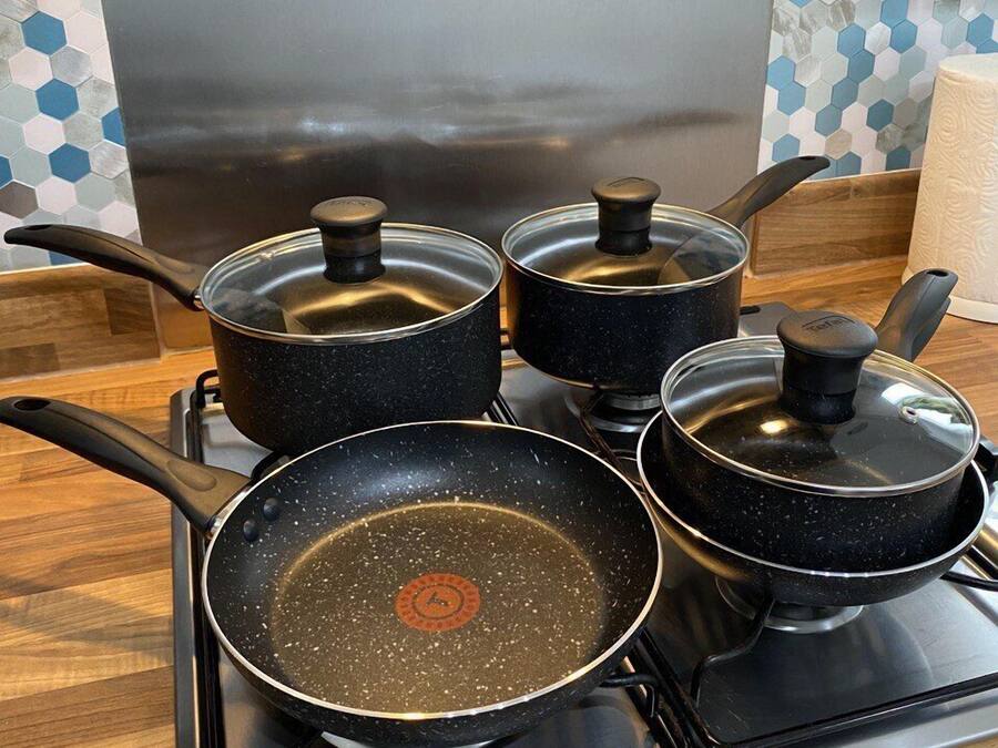 Four black pots with lids on a stove.