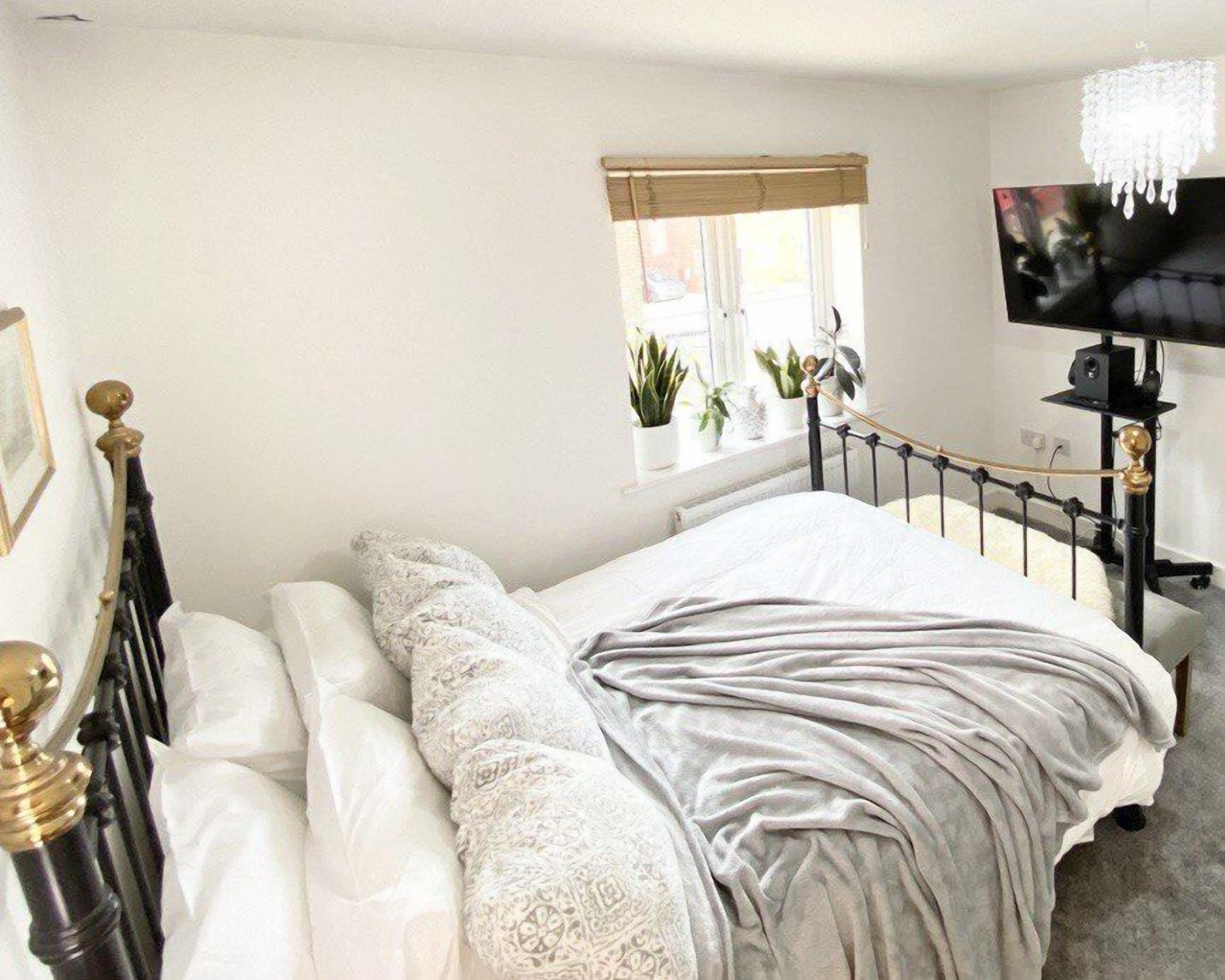 A bedroom with a bed, a window with plants, a TV, and a chandelier.