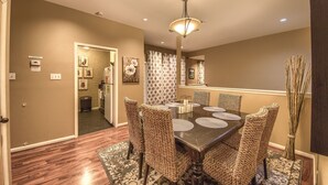 A dining area with a round table, six wicker chairs, and a chandelier.