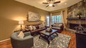 A living room with a ceiling fan, a fireplace, and a large window with curtains.