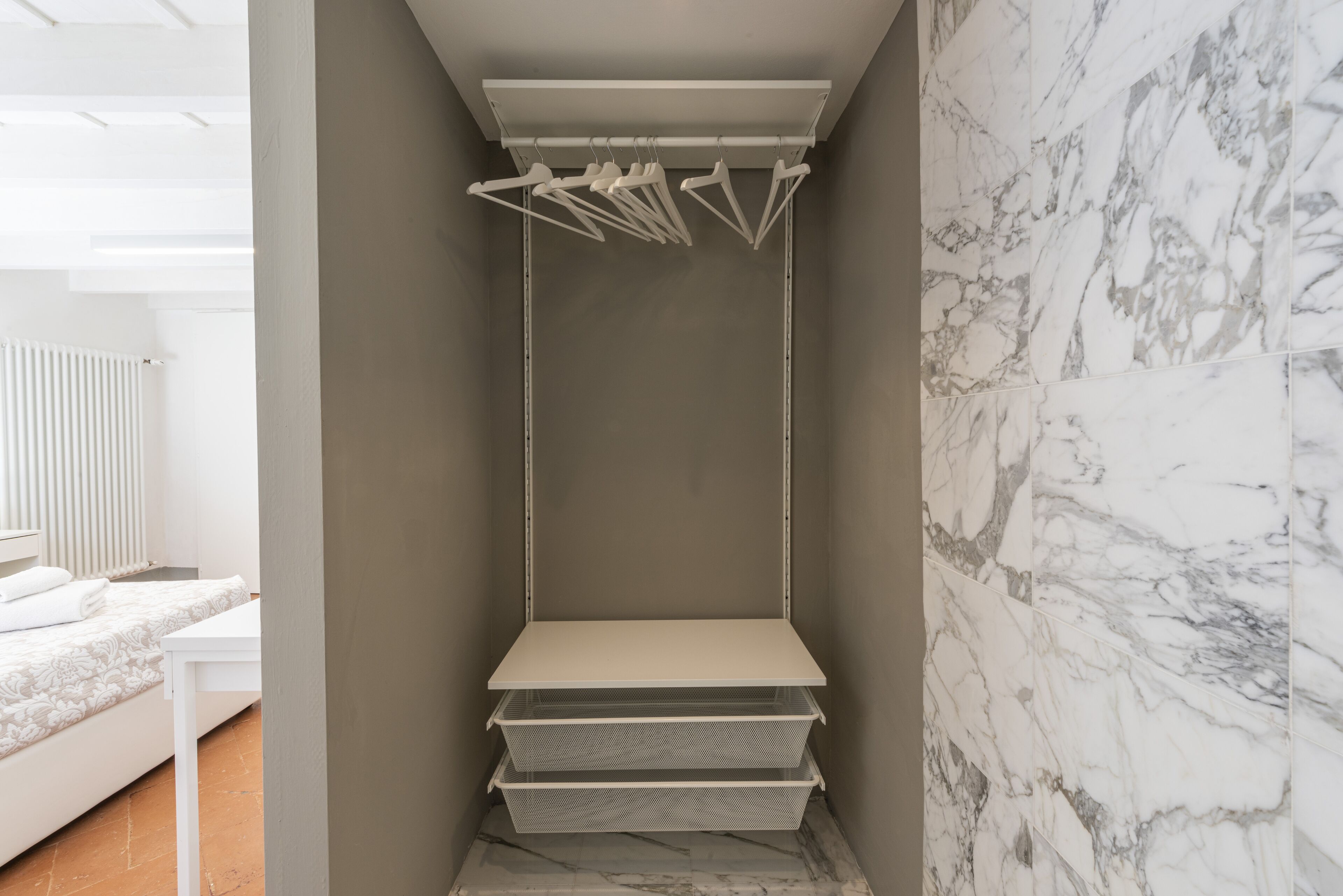 A corner of a room with a bed, a white shelf unit, and a marble wall.