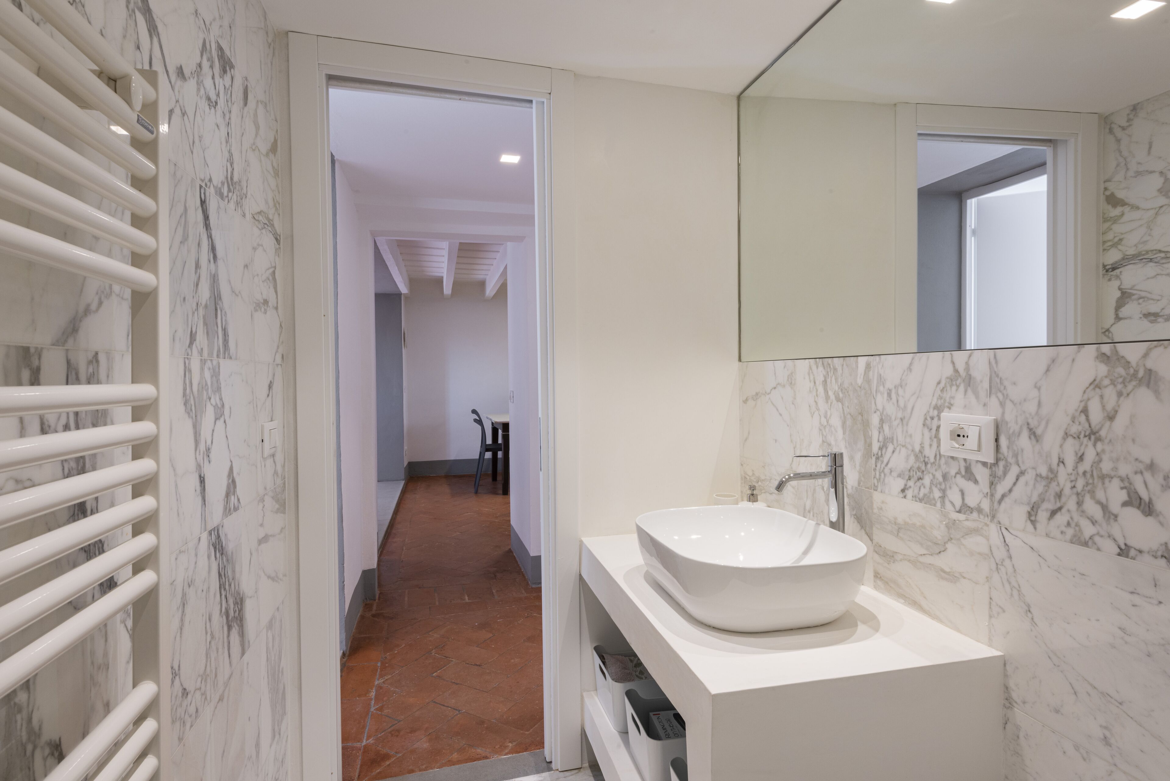 A modern bathroom with a white sink, marble walls, and a hallway leading to another room.