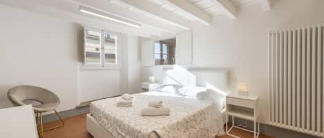 Un dormitorio moderno con cama, mesita de noche, silla y radiador.