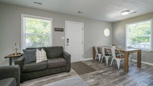 Un salon avec un canapé gris, une table à manger avec des chaises blanches et une porte.