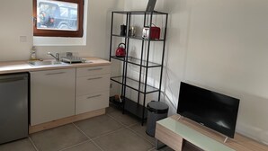 Eine kleine Küche mit Spüle, Arbeitsplatte, einem Holzkorpus, einem schwarzen TV-Schrank und einem Fenster mit Blick auf ein geparktes Fahrzeug.