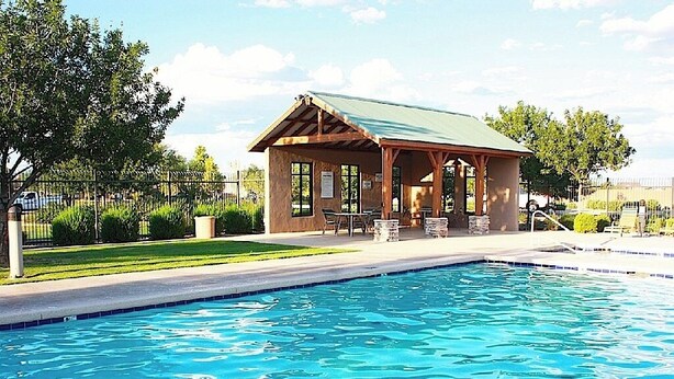 Un área de piscina con un pabellón cubierto, una piscina cristalina y un jardín vallado.