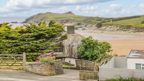 A coastal property with a stone house, a wooden gate, and a view of the beach and cliffs. - Porth Beach (Newquay)
