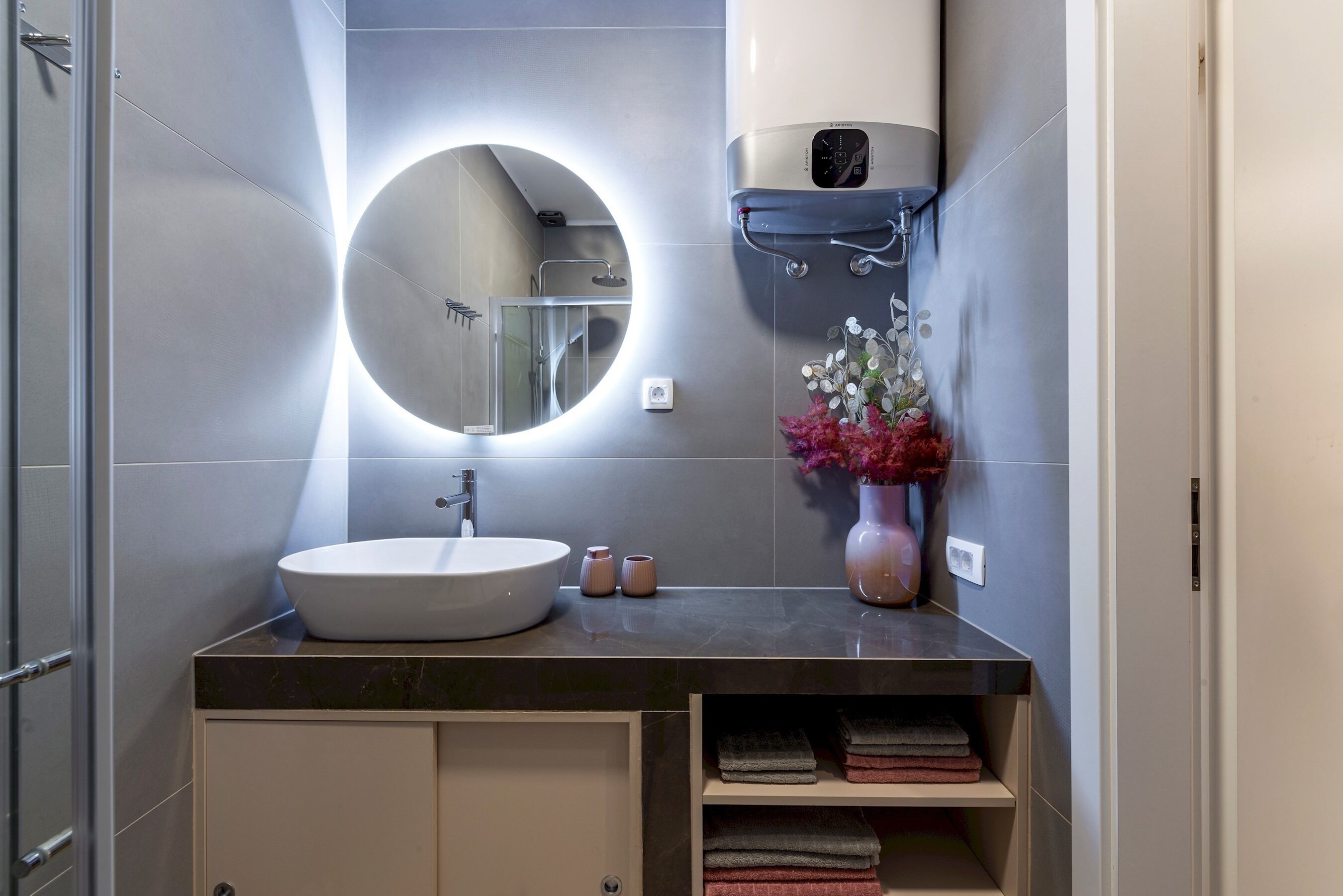 Ein modernes Badezimmer mit rundem Spiegel, Waschbecken und Handtuchhalter.