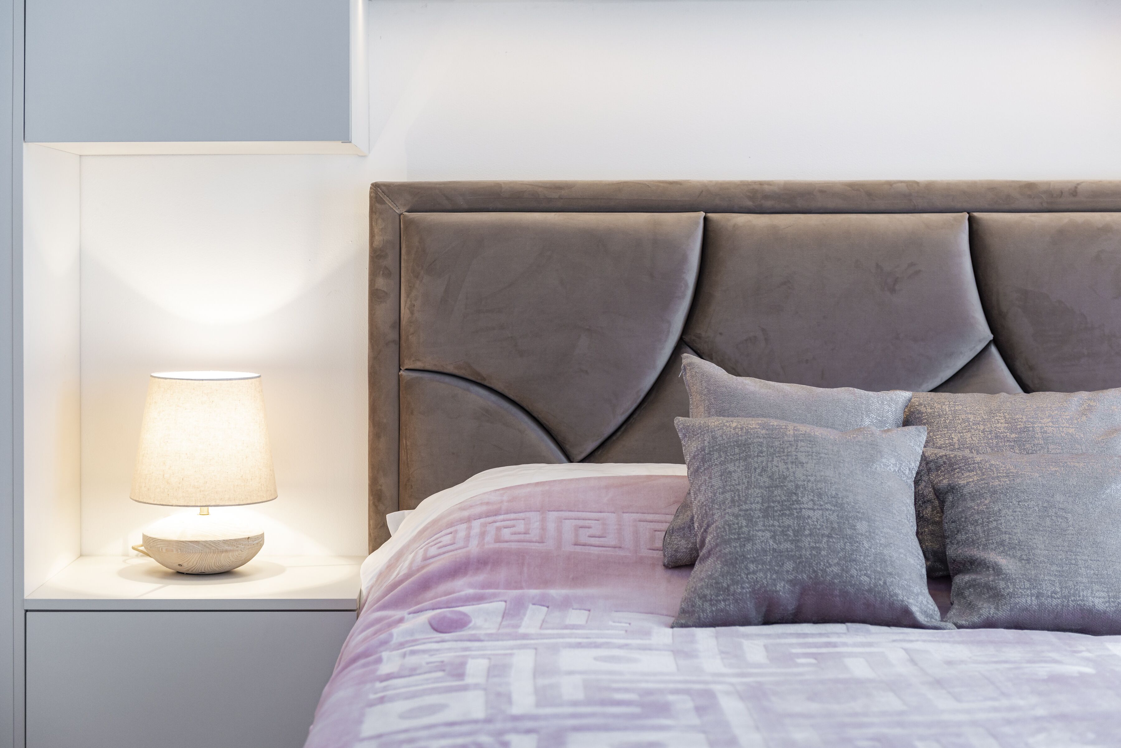 A neatly made bed with a headboard, a bedside lamp, and pillows.