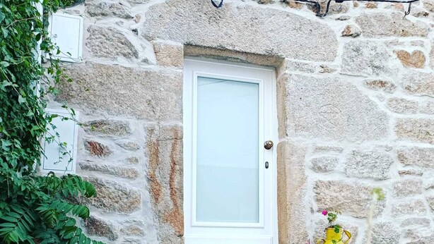 A stone building with a white door, potted plants, and a concrete pathway. - Casa Darcã (Alijó)