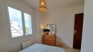 A bedroom with a bed, a dresser, a mirror, a small stool, and a door.