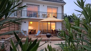 A two-story house with a balcony, a patio with outdoor furniture, and a barbecue grill.
