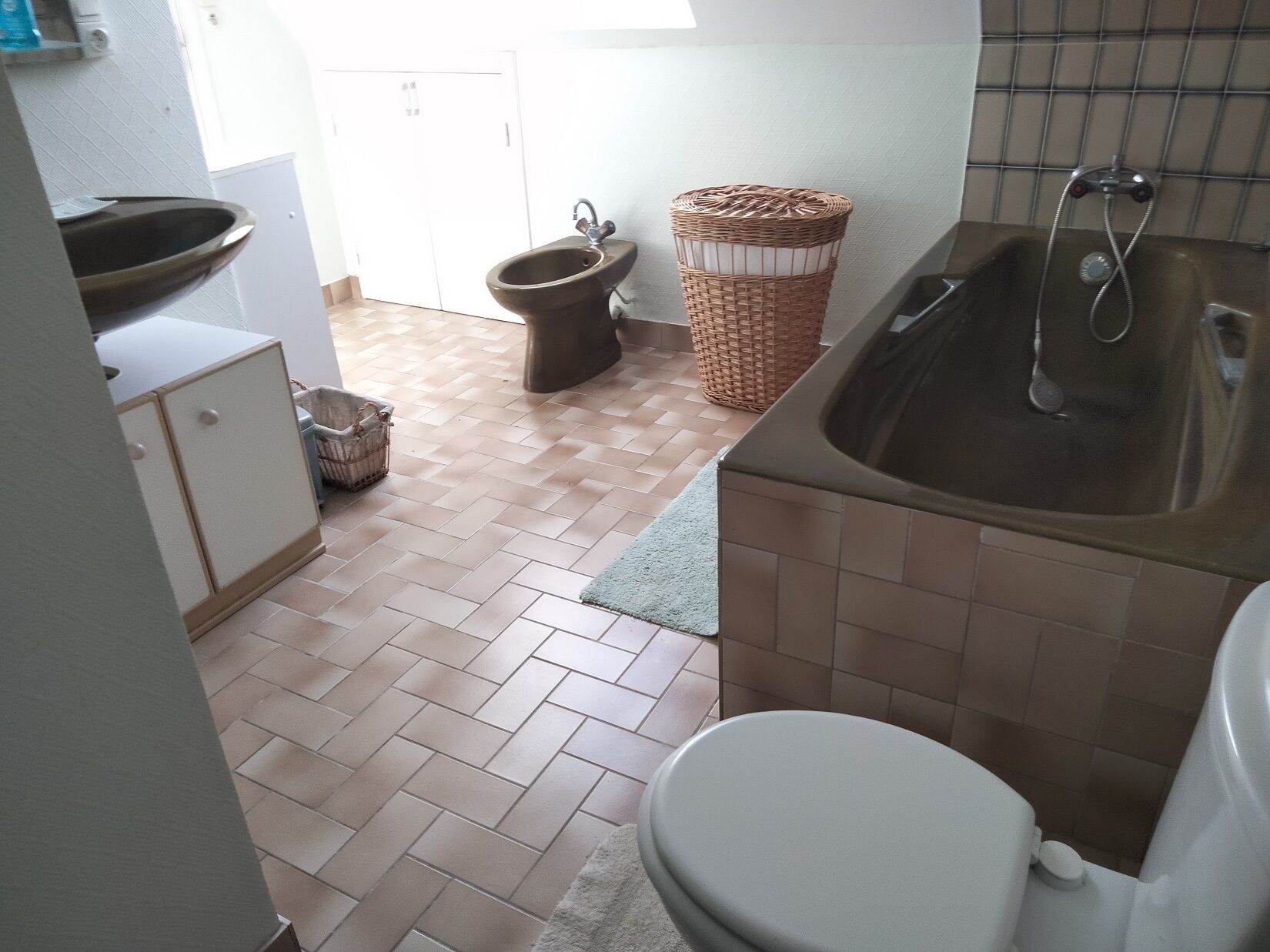 Een badkamer met een wastafel, toilet en bidet. Er staat een rieten mand en de vloer is betegeld.