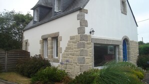 A two-story house with a stone facade, a blue door, and a small garden in front.