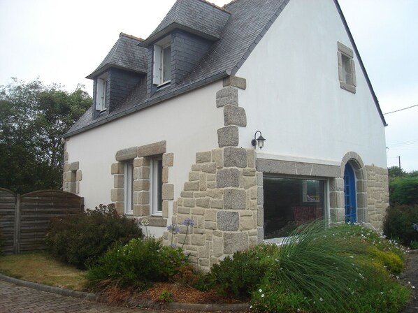A two-story house with a stone facade, a blue door, and a small garden in front.