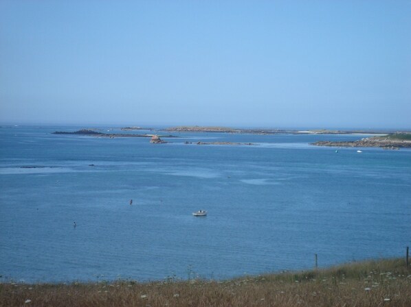 A coastal view with calm waters, a small boat, and distant rocky outcrops.