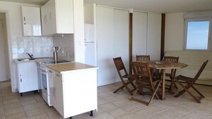 Uma cozinha compacta com armários brancos, um fogão e uma pia. Há uma mesa de jantar com quatro cadeiras e uma janela com vista.