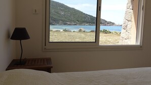 Quarto com cama, luminária de cabeceira e janela com vista para a paisagem costeira.