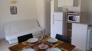 Um espaço compacto com mesa de jantar para quatro pessoas, um sofá branco, área de cozinha com micro-ondas e geladeira.