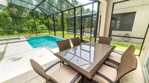 A glass-enclosed patio with a pool, outdoor seating, and a view of the surrounding greenery.