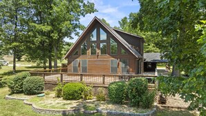 Une cabane en bois dotée d’une grande terrasse, entourée d’arbres et d’un jardin bien entretenu.
