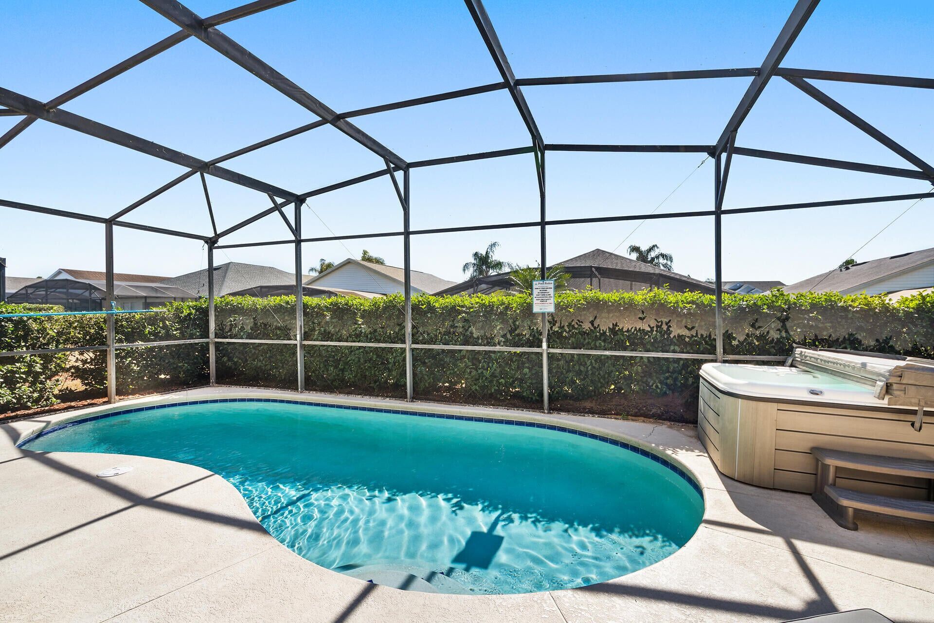 Une piscine à bordures courbes, entourée d’une clôture métallique, et un jacuzzi situé à droite.