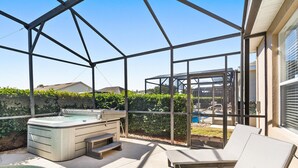 A covered outdoor area with a hot tub, lounge chairs, and a pool.